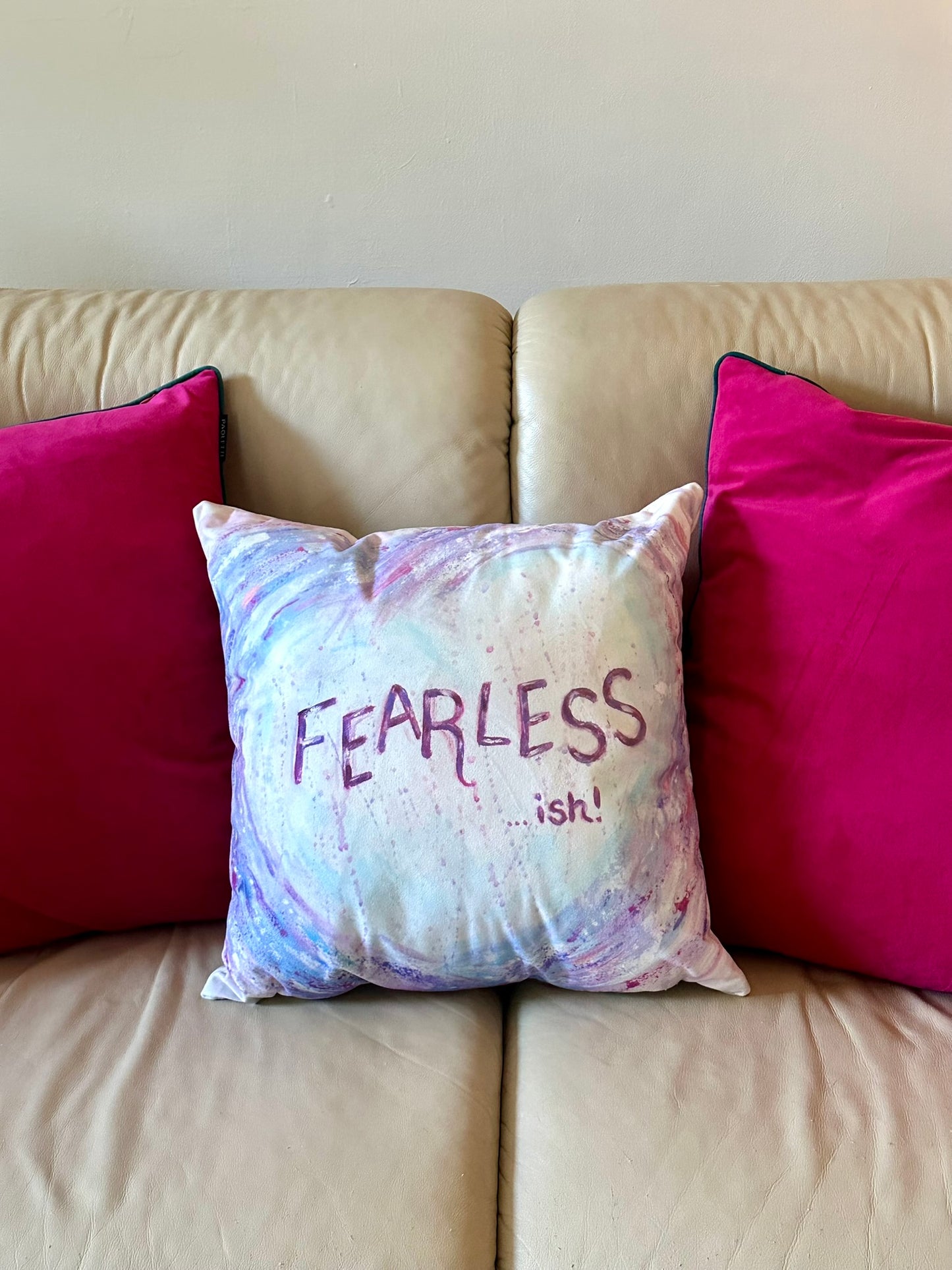 Fearless-ish cushion by Julie Hogarth-Jones styled on a cream sofa with bright pink cushions.