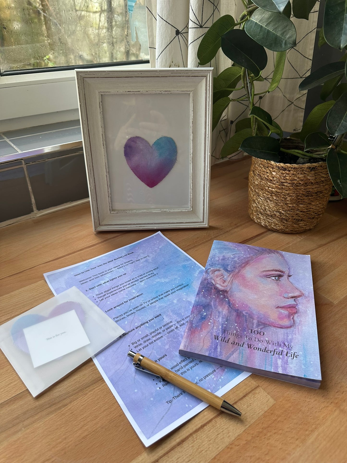 Into The Wild Rediscovery Box by Julie Hogarth-Jones - contents including bucket list book, pen, hand-painted heart in an envelope and how to start guide laid out on a wooden surface. 